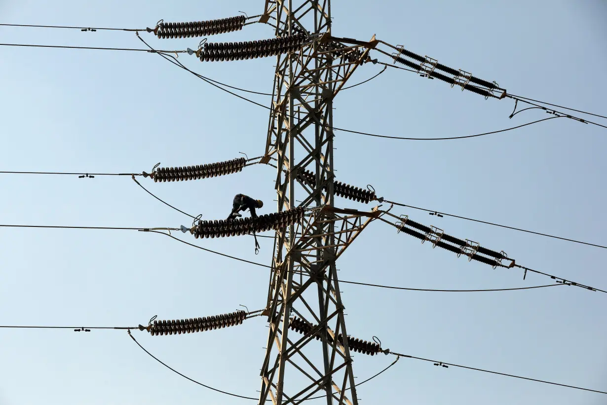 A technician works on porcelain insulators on power transmission tower in Karachi