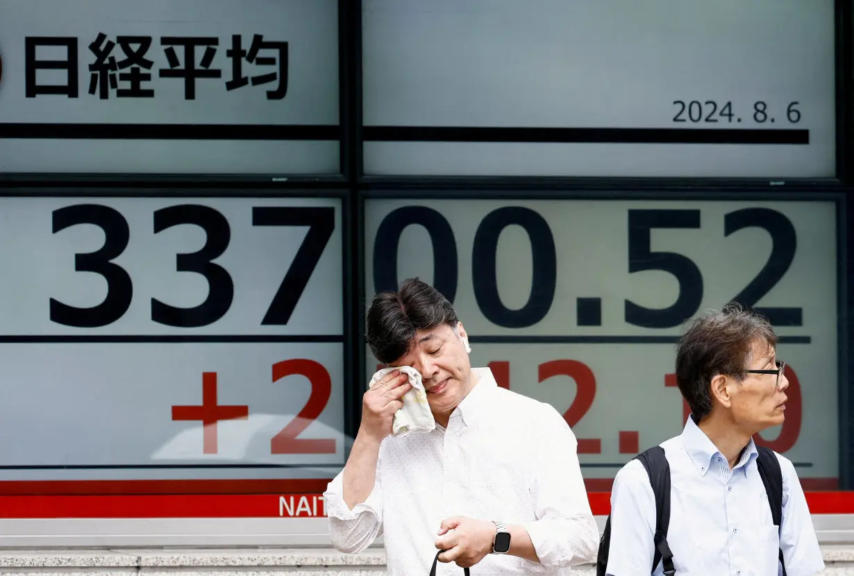 FILE PHOTO: A passerby gestures in front of an electronic board displaying the Nikkei stock average outside a brokerage in Tokyo