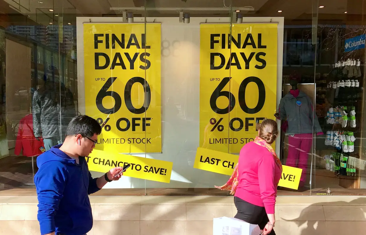 FILE PHOTO: Shoppers walk past sales signs on display in the window of a retail store at a shopping mall in Sydney