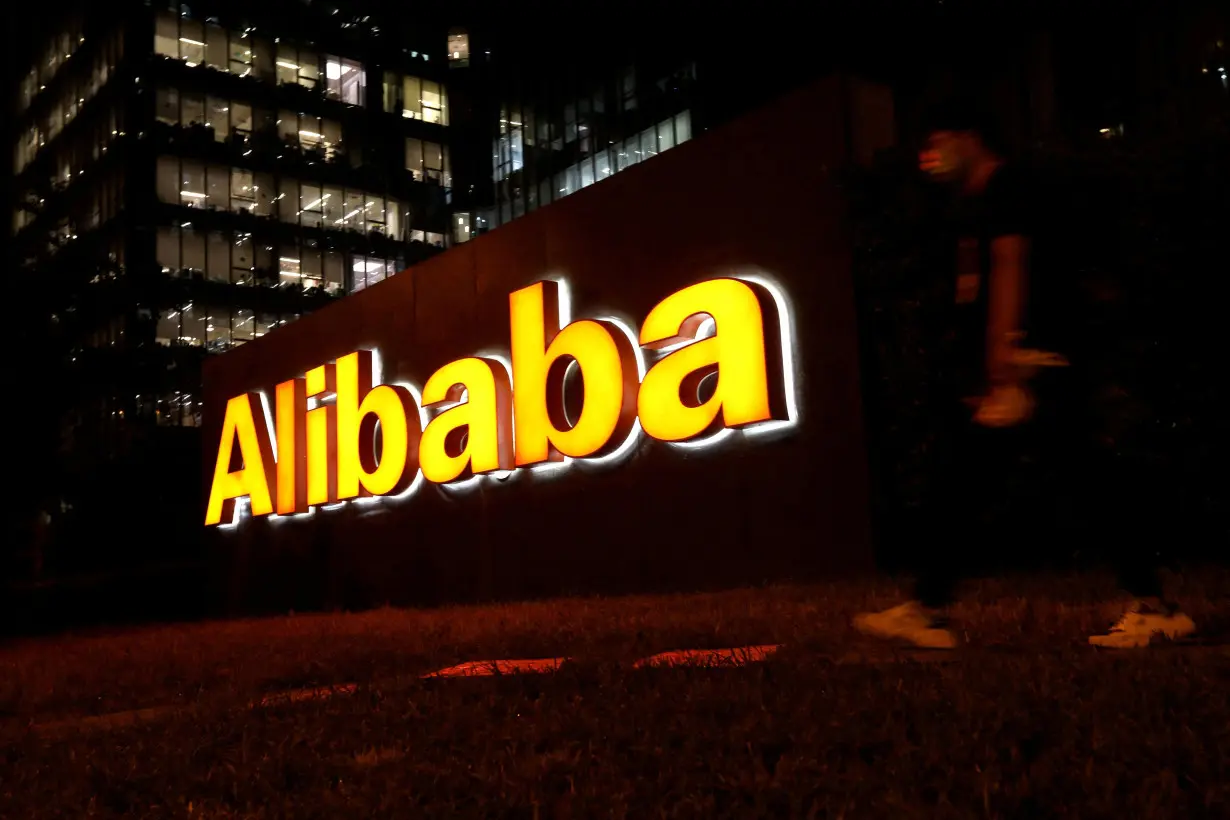 FILE PHOTO: FILE PHOTO: Man walks past a logo of Alibaba Group at its office building in Beijing