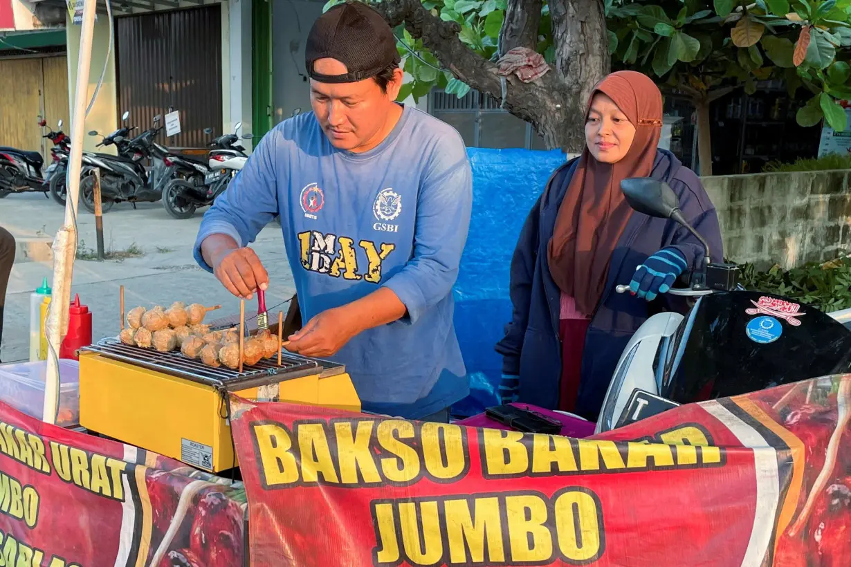 Rahmat Hidayat, 44, serves a customer as he grills meatball after losing his job when the shoe factory he worked for closed down last year in Karawang