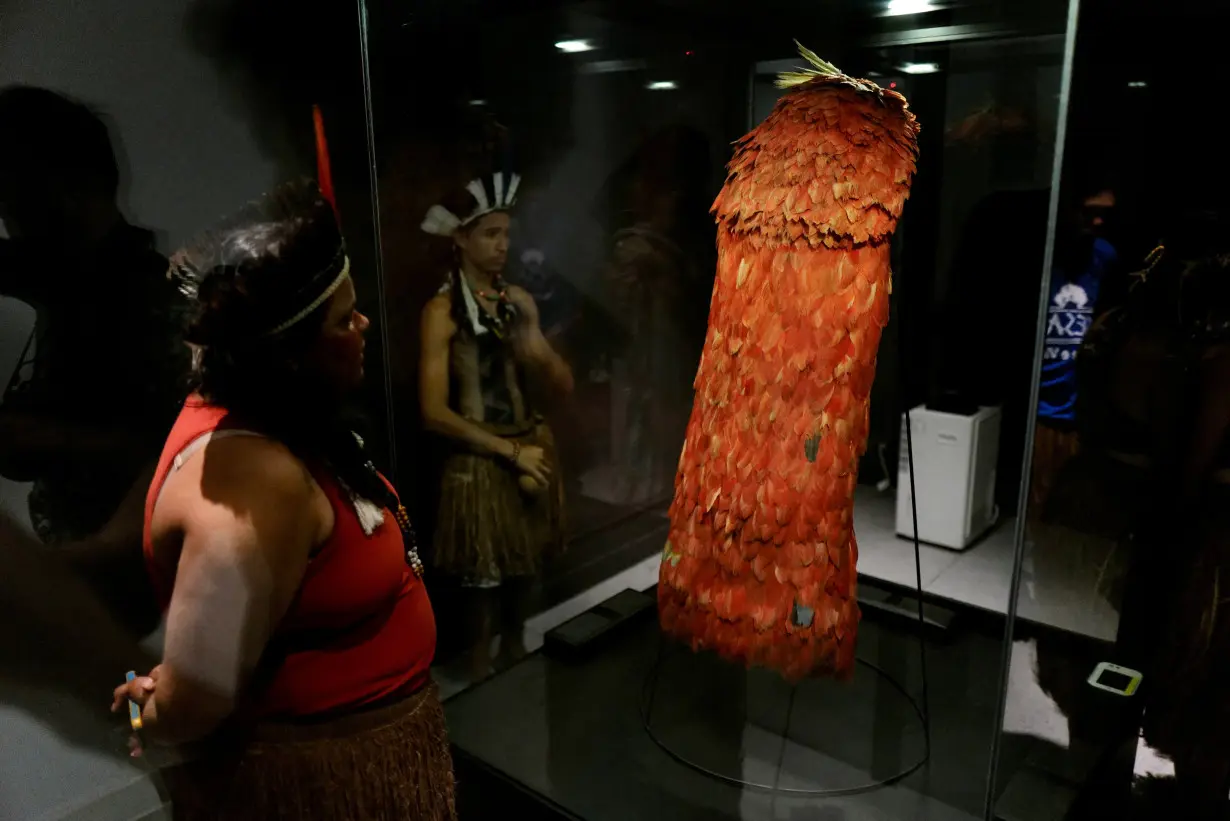 Indigenous people stand next to the Tupinamba cloak, a feathered ceremonial cape used in religious rituals, at the Brazil's National Museum in Rio de Janeiro