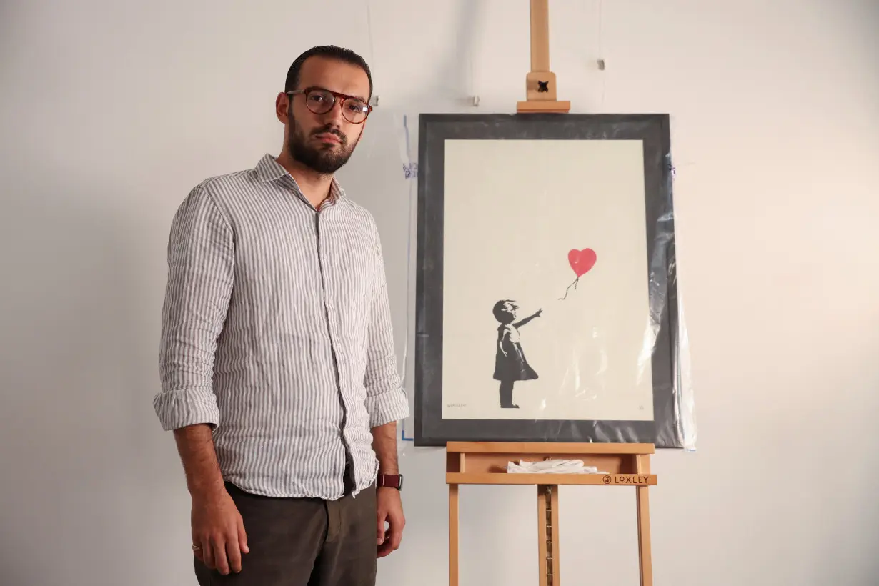 Gallery manager Lindor Mehmetaj poses for a photo next to Banksy's 'Girl with Balloon', in London