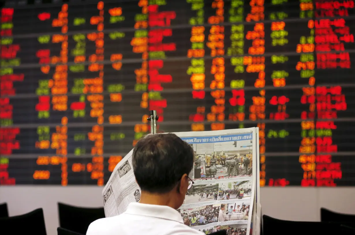 A Thai investor reads a newspaper in front of an electronic board displaying live market data at a stock broker's office in central Bangkok