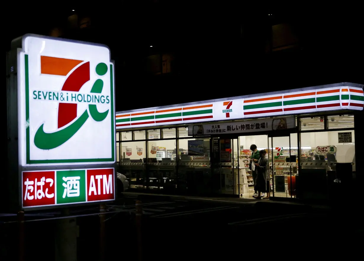 FILE PHOTO: Shoppers walk out from a 7-Eleven convenience store in Tokyo