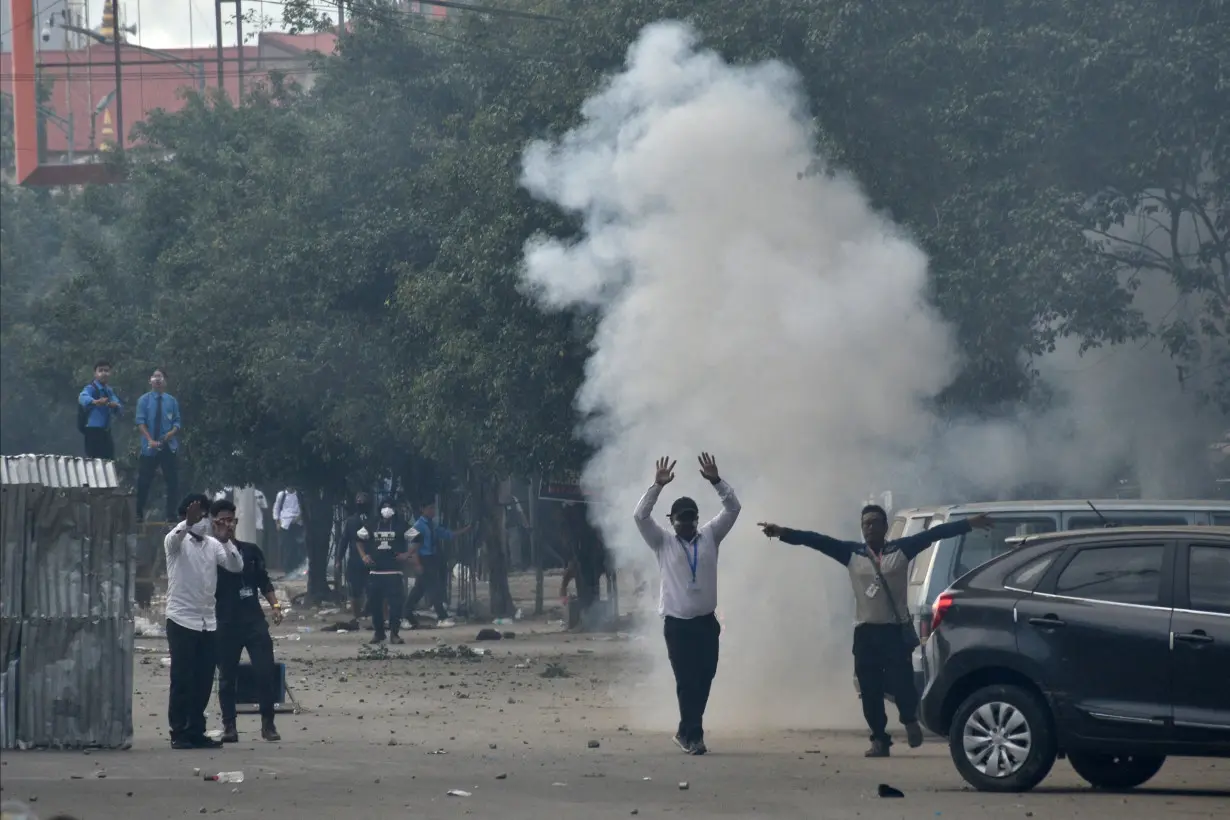 Demonstrators react as smoke billows from a tear gas shell fired by police to disperse the protesters, in Imphal