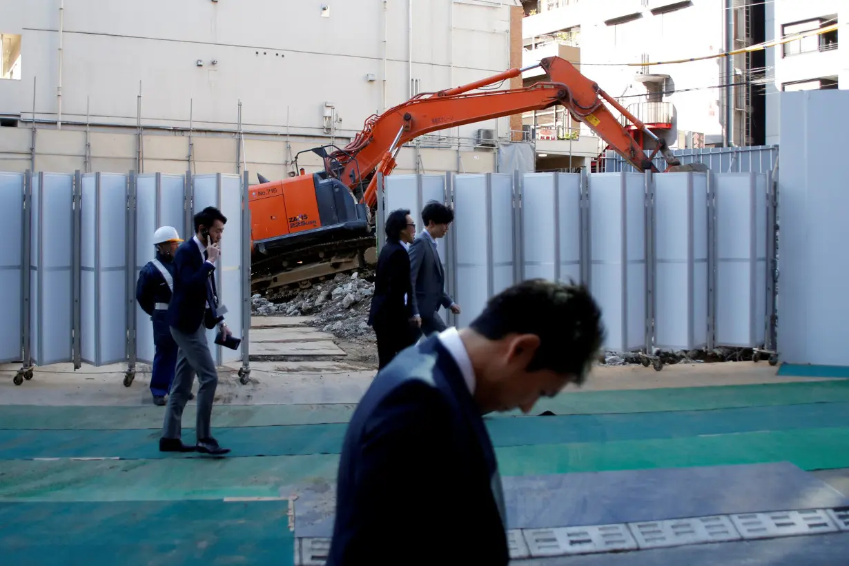 FILE PHOTO: Businessmen walk past heavy machinery at a construction site in Tokyo's business district