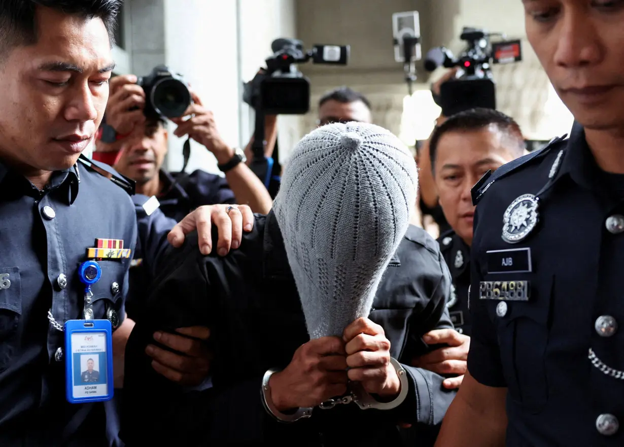 A man linked to Global Ikhwan Service and Business Holdings (GISB) covers his face as he is escorted by police officers after being charged in a court in Putrajaya