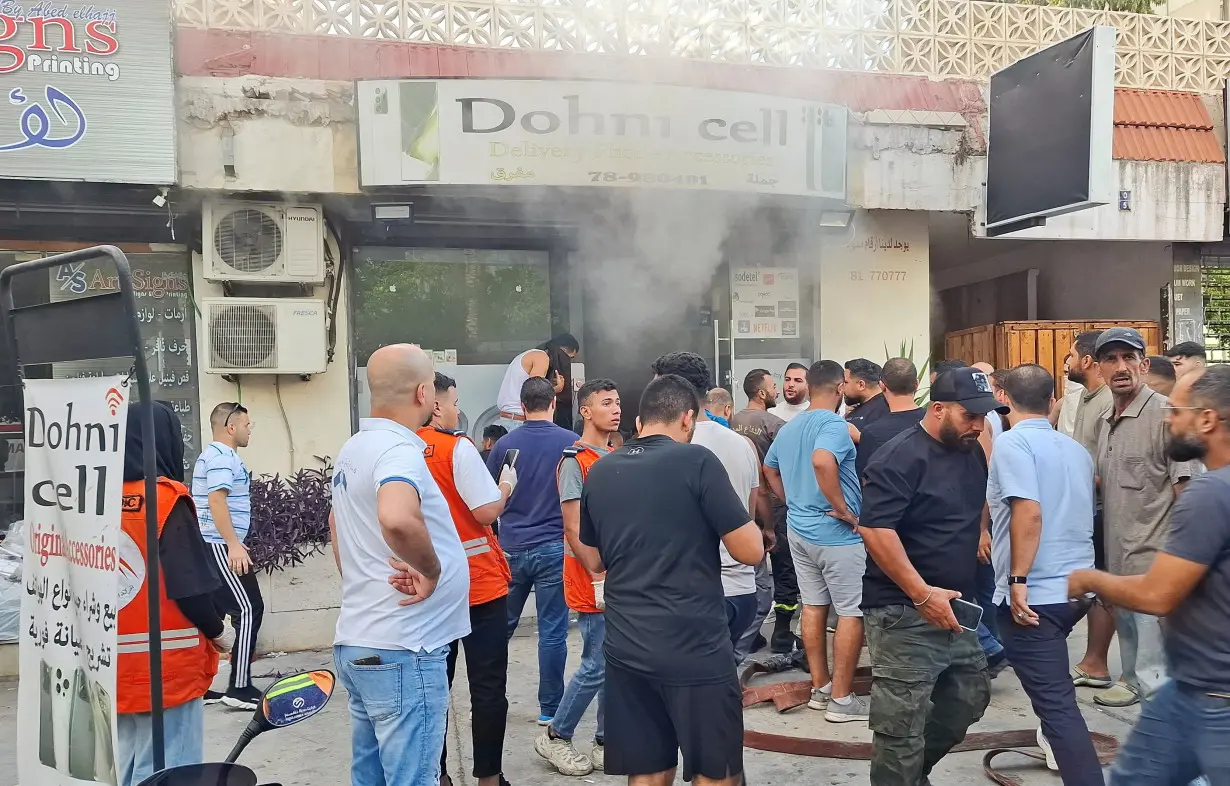 People gather as smoke rises from a mobile shop in Sidon