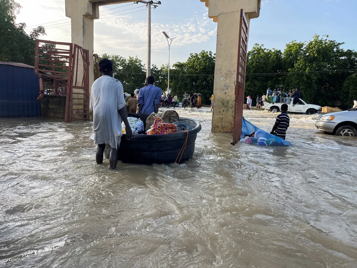 Flood victims push their belongings along a flooded road as they move to safety, in Maiduguri