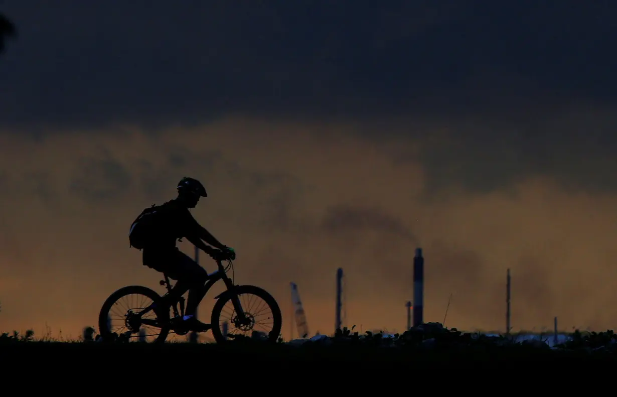 FILE PHOTO: A man cycles past a chimney giving off emissions in an industrial area of Singapore