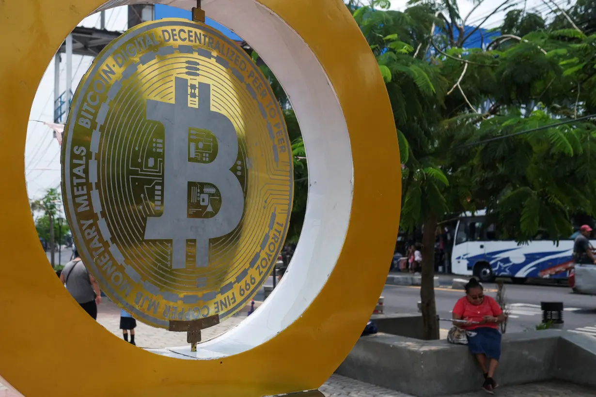 A woman sits by a Bitcoin sign at the Bitcoin Plaza, in Ilopango