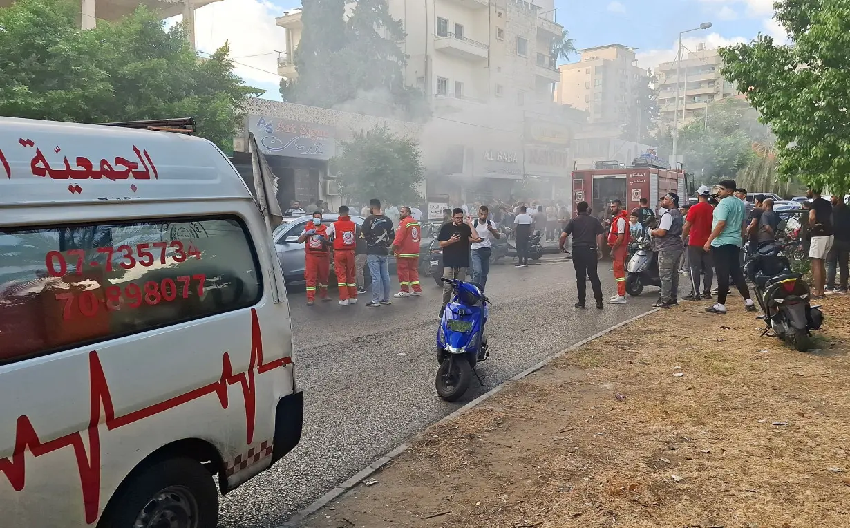 Smoke rises from a mobile shop as civil defence members gather in Sidon