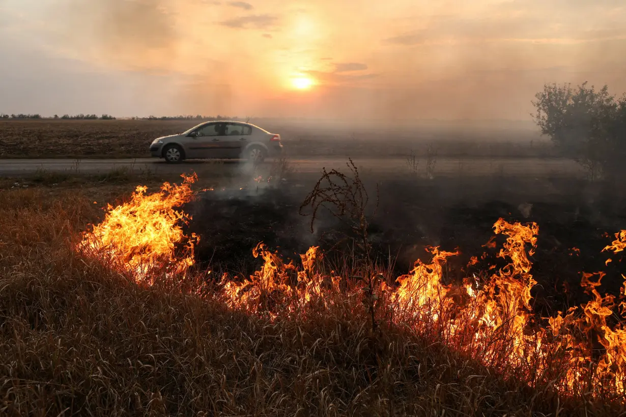 Person drives a car along a road while roadside burns after a Russian military strike outside the town of Pokrovsk