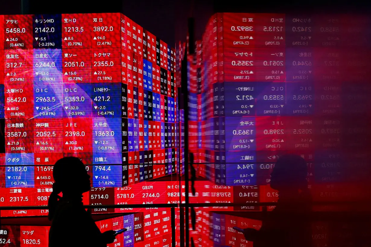 A visitor stands next to an electronic screen displaying Japan's Nikkei stock prices quotation board in Tokyo