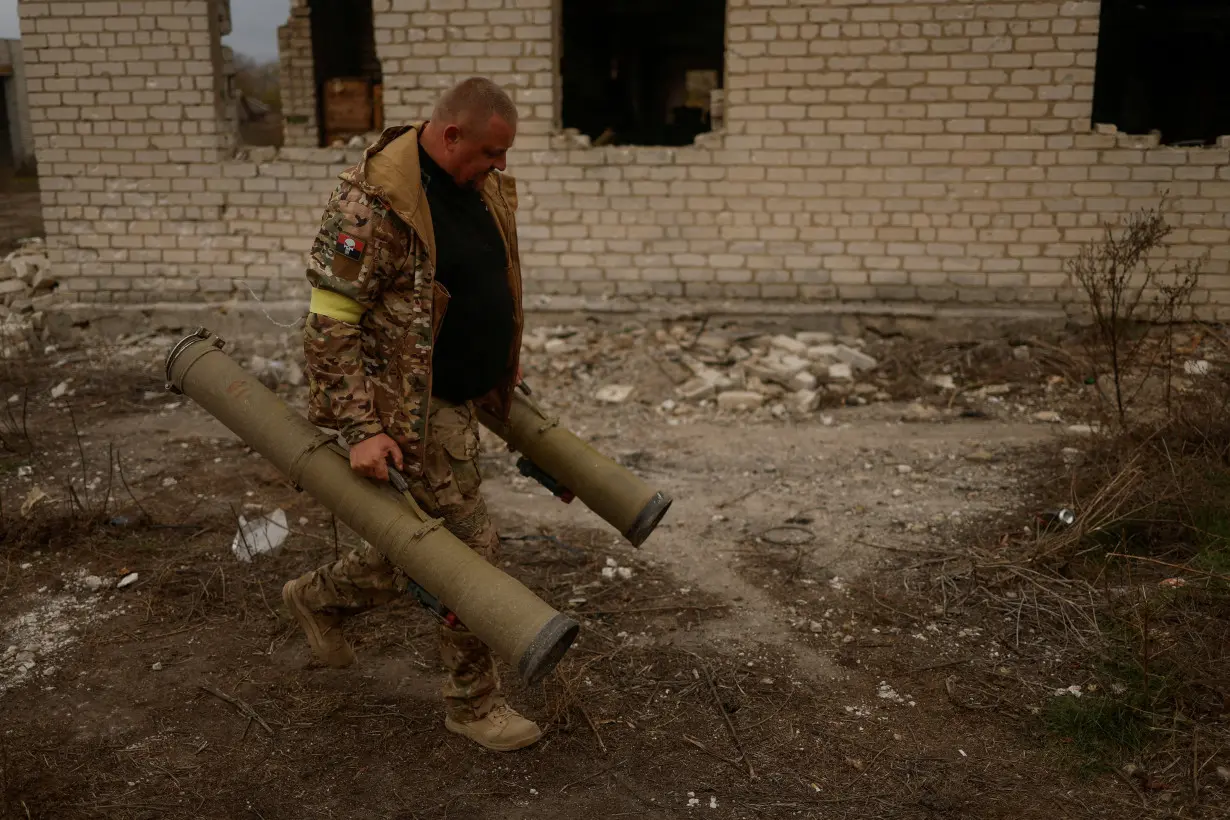 Ukrainian serviceman carries captured anti-tank grenade launchers at a former position of Russian soldiers in the village of Blahodatne in Kherson region