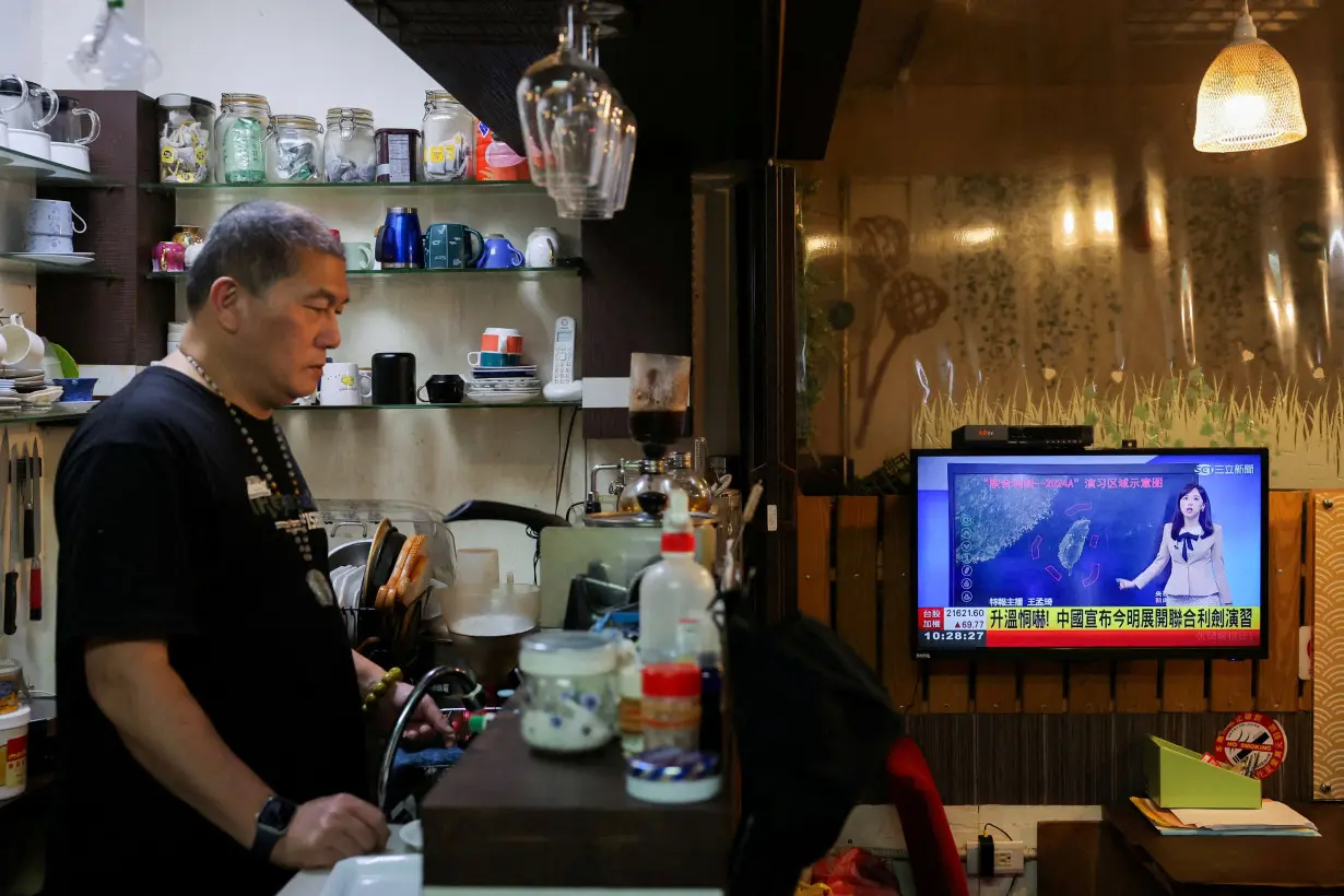 FILE PHOTO: A person stands in a cafe as a news broadcast shows China announcing new military drills around Taiwan, in Keelung