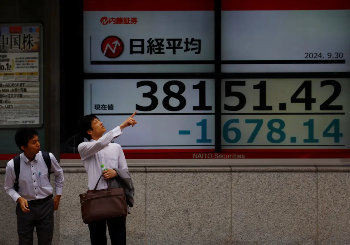 Passersby chat in front of an electric board displaying the Nikkei stock average outside a brokerage in Tokyo