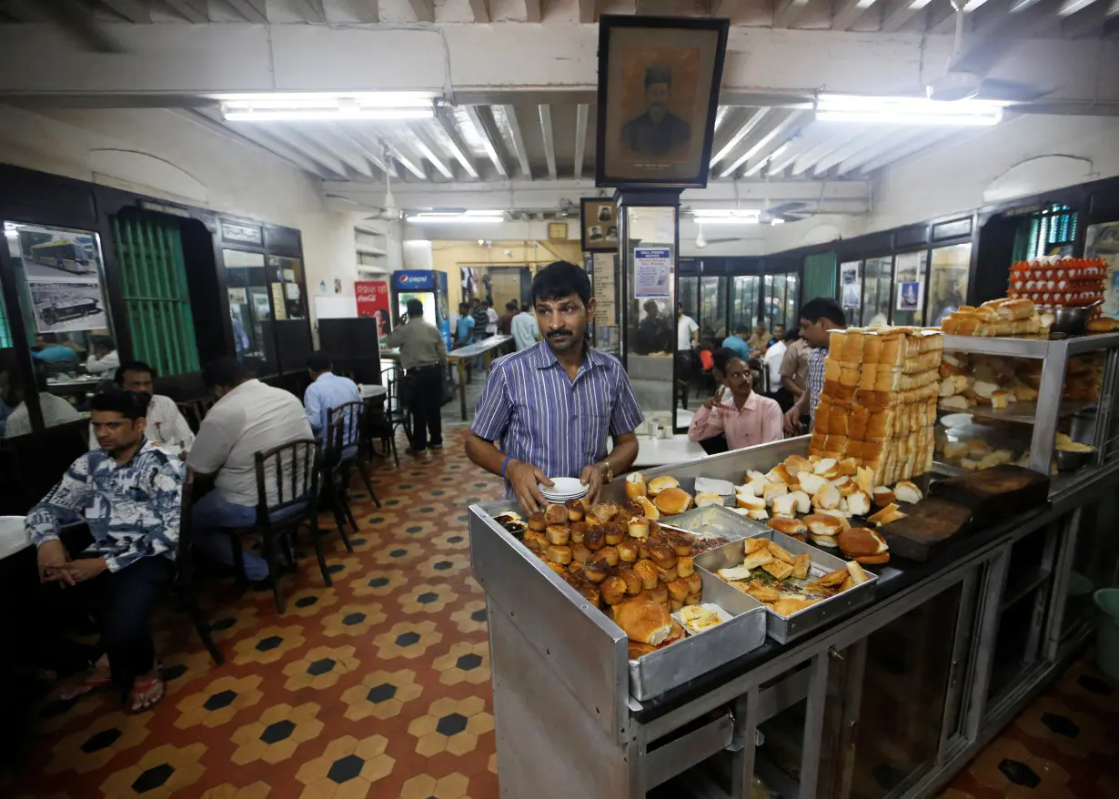 A waiter arranges plates at a counter stacked with breakfast items at an Iranian Parsi restaurant in Mumbai