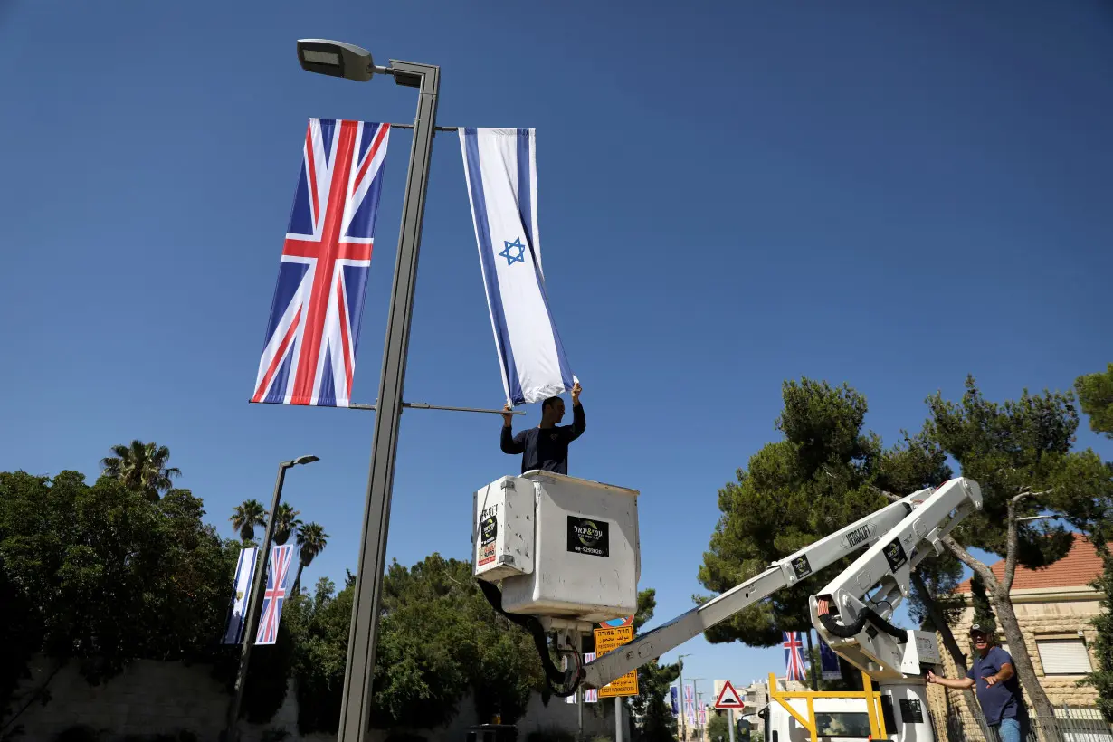 A Jerusalem municipality worker hangs an Israeli flag next to the British flag, the Union Jack, as he stands on a platform near Israel's presidential residence in Jerusalem ahead of the upcoming visit of Britain's Prince William