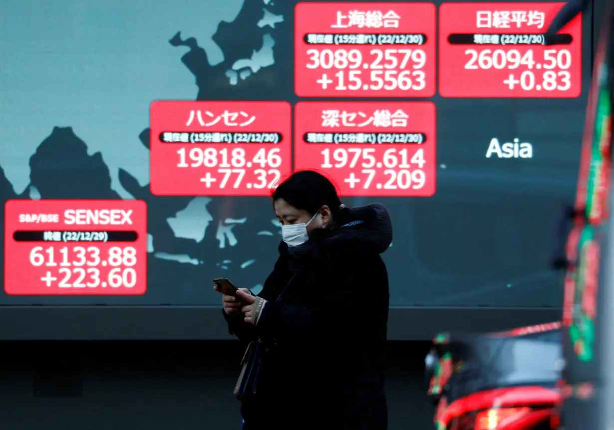 FILE PHOTO: A passerby walks past an electric screen displaying various Asian countries' stock price indexes outside a brokerage in Tokyo