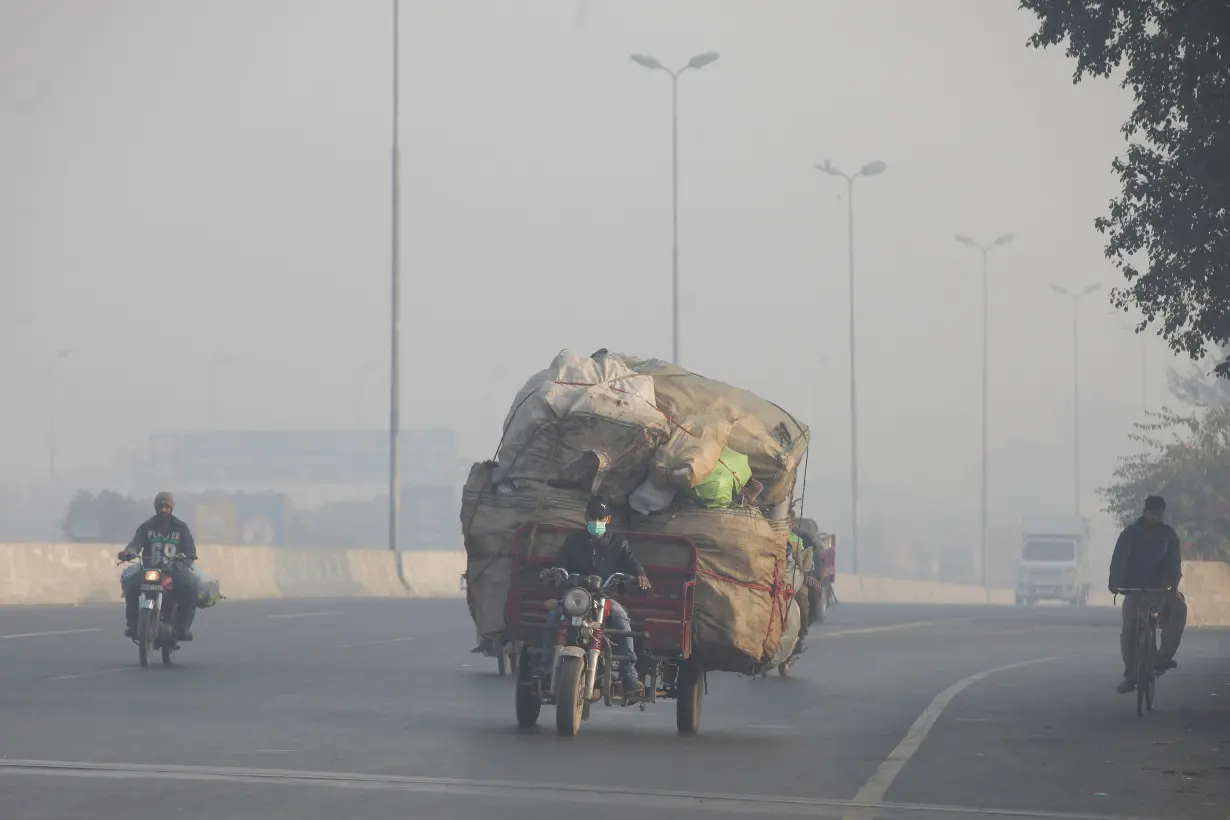 Man rides a motor tricycle, loaded with sacks of recyclables, amid dense smog in Lahore