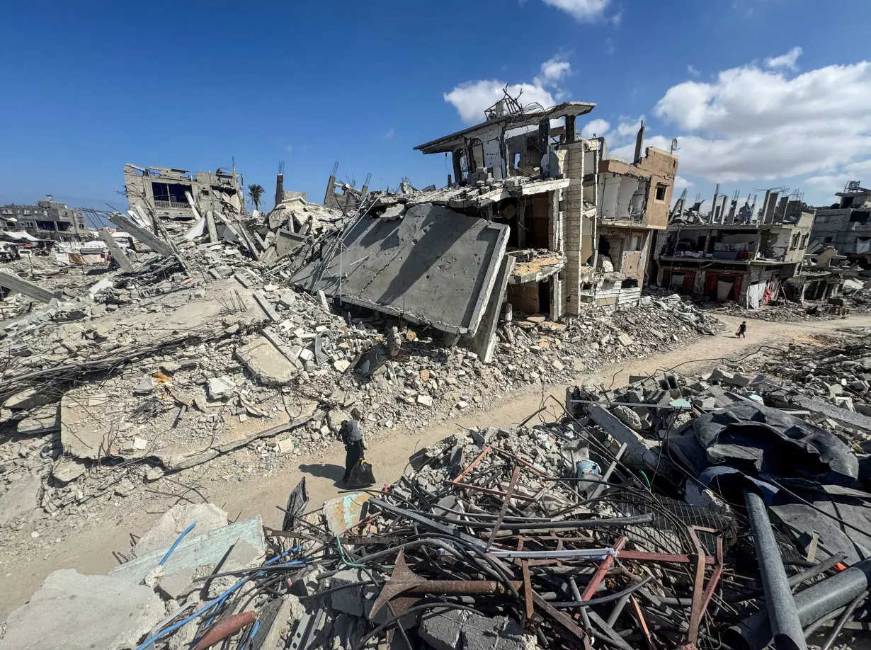 Palestinians walk near rubble and destroyed buildings, in Khan Younis