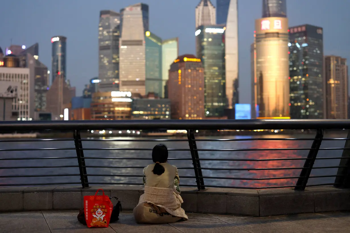 Woman sits one the Bund near Huangpu river as she looks on the financial district of Pudong in Shanghai