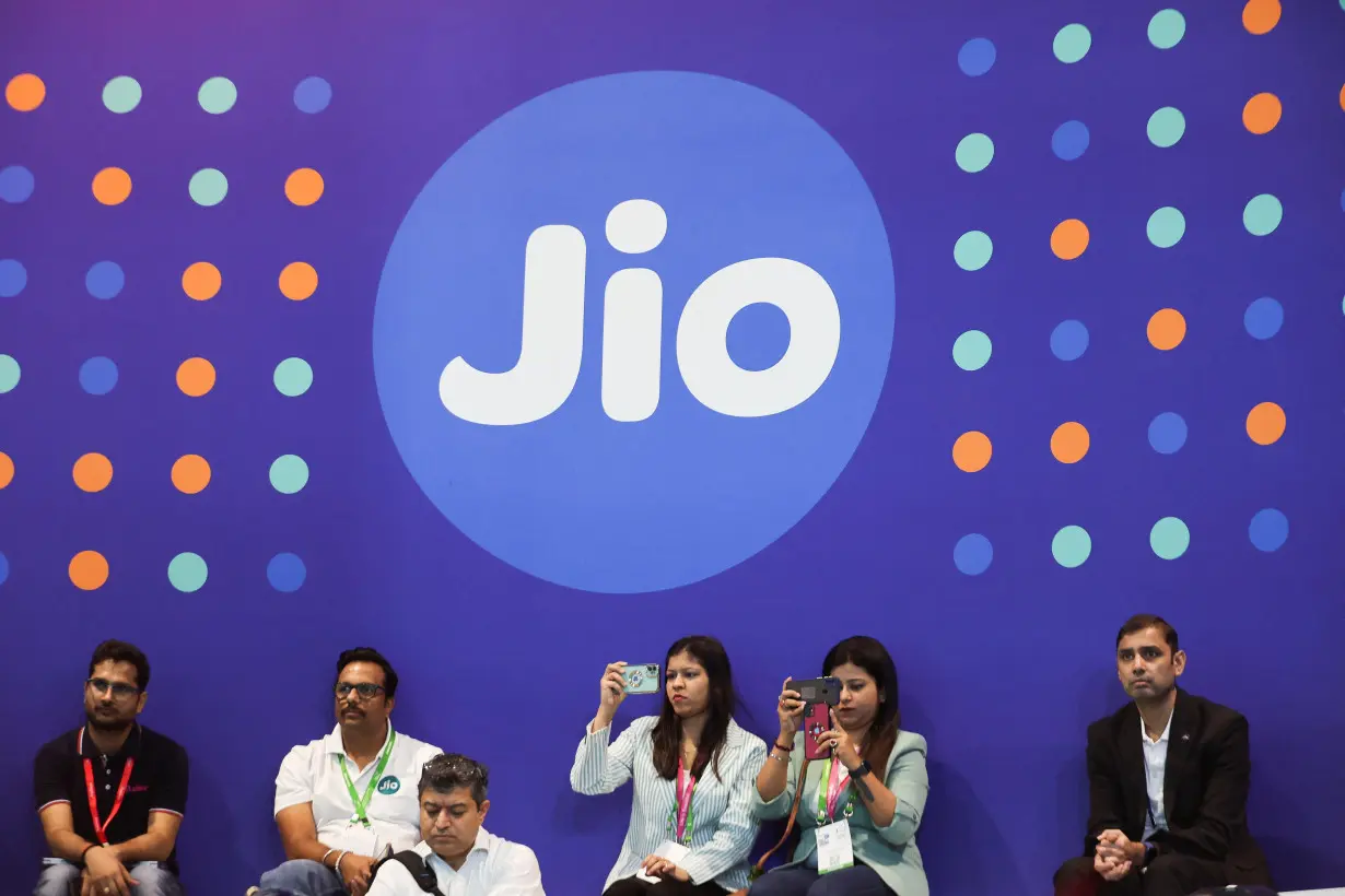 People take pictures with their mobile phones in front of a board with the logo of Jio at the ongoing India Mobile Congress 2022, at Pragati Maidan, in New Delhi