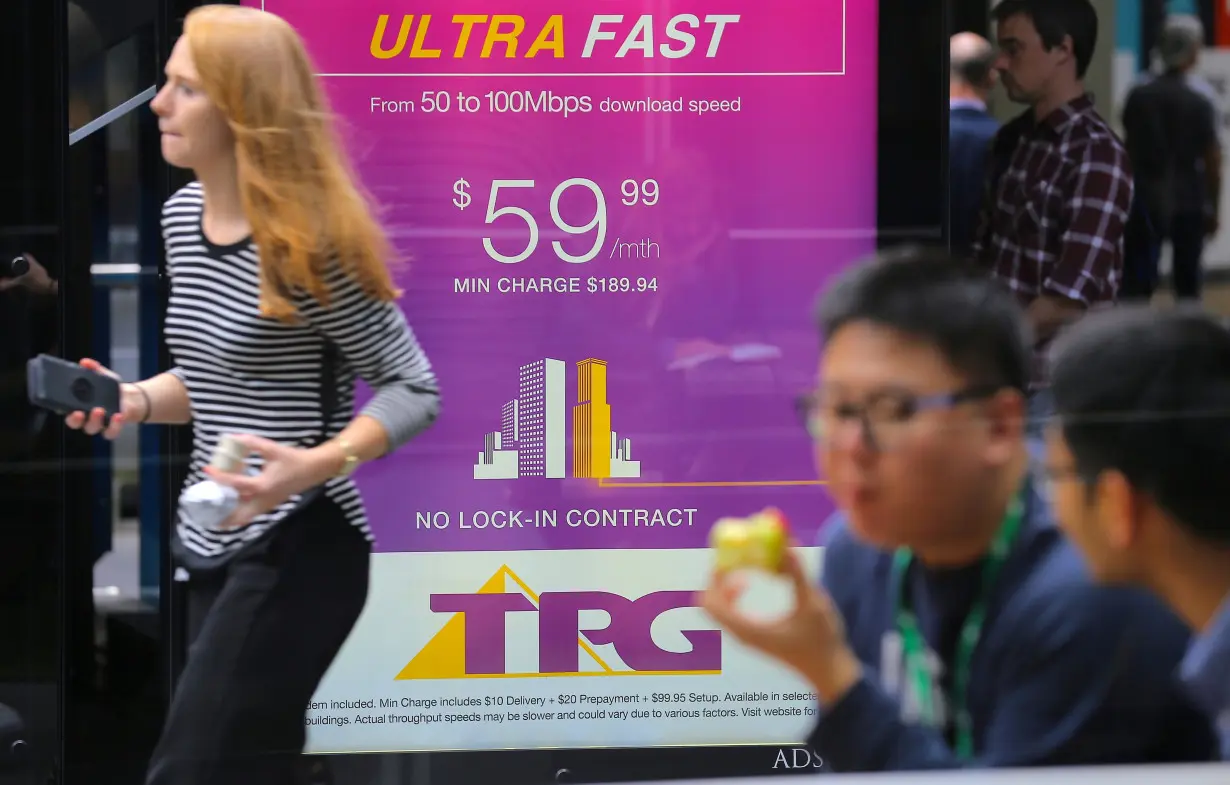 A woman looks at her phone as she walks past an advertisement for Australia's TPG Telecom Ltd in central Sydney, Australia