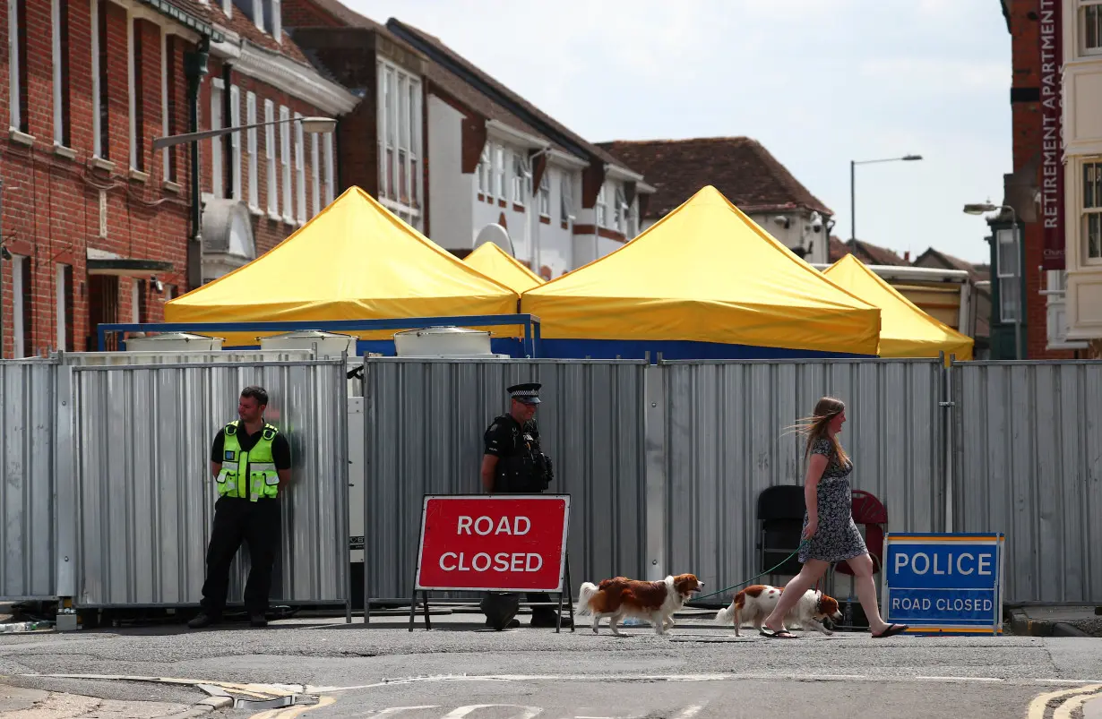 FILE PHOTO: A woman walks her dogs past police officers stationed outside barriers blocking the street where Dawn Sturgess lived before dying after being exposed to a Novichok nerve agent, in Salisbury