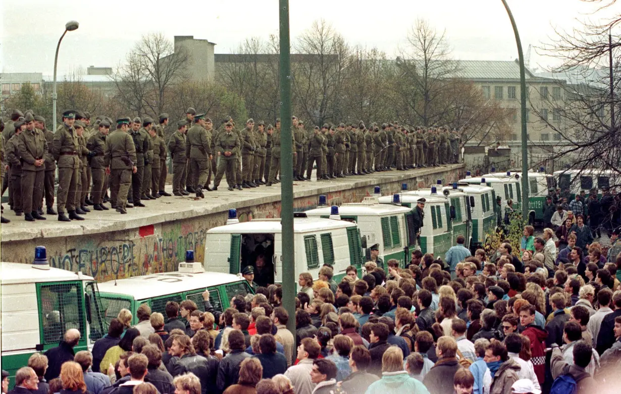 FILE PHOTO: East Berlin border guards stand atop the Berlin Wall at the Brandeburg Gate faced by thousands of West Berliners on November 11, 1989.