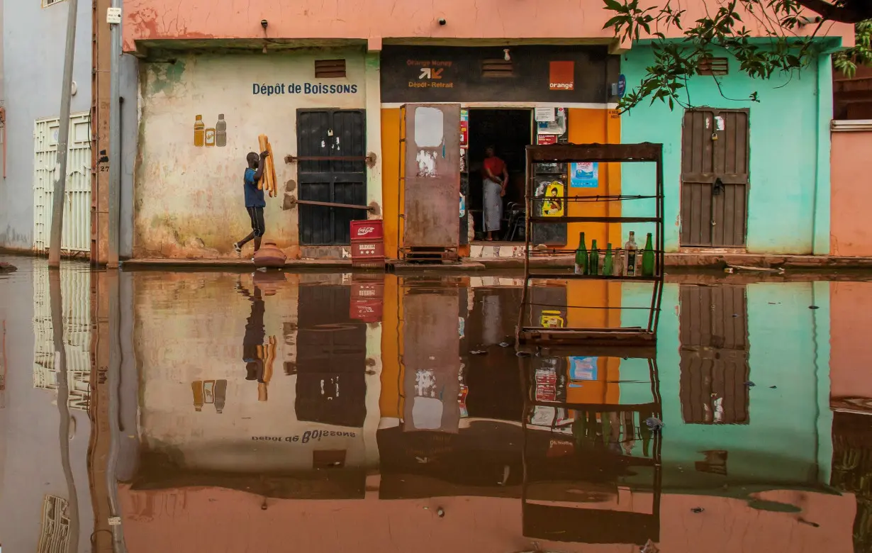 A man carries bread as he walks towards a grocery store, on a flooded street in Bamako