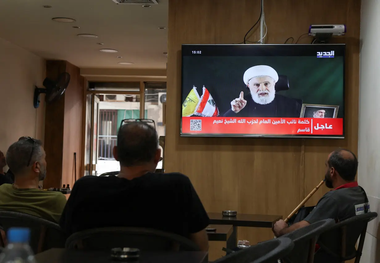 People watch Hezbollah deputy leader Sheikh Naim Qassem delivering a televised address, as they sit in a cafe in Beirut