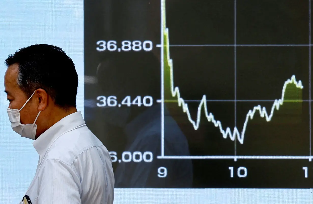 FILE PHOTO: A passerby walks past in front of an electronic screen displaying the graph showing today's movements of Japan's Nikkei share average in Tokyo