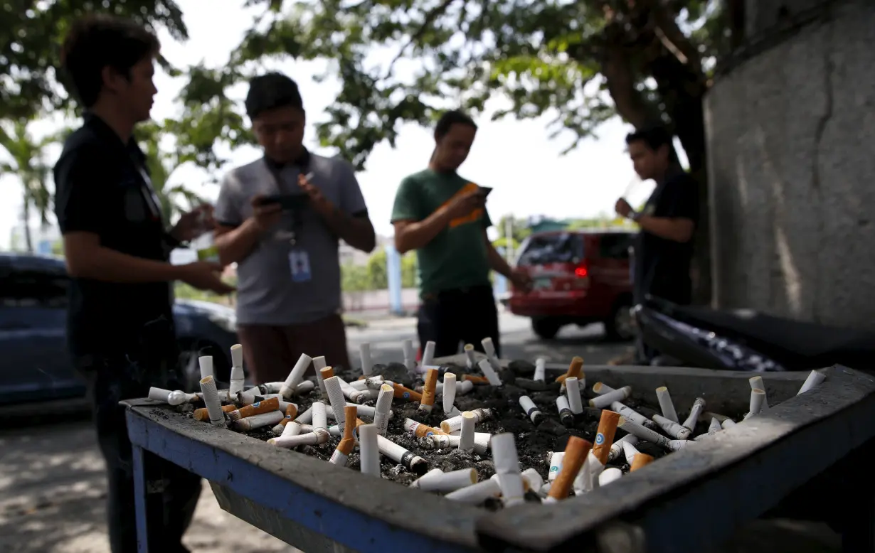 Men smoke cigarettes near a tray filled with stubs beside a road in Las Pinas