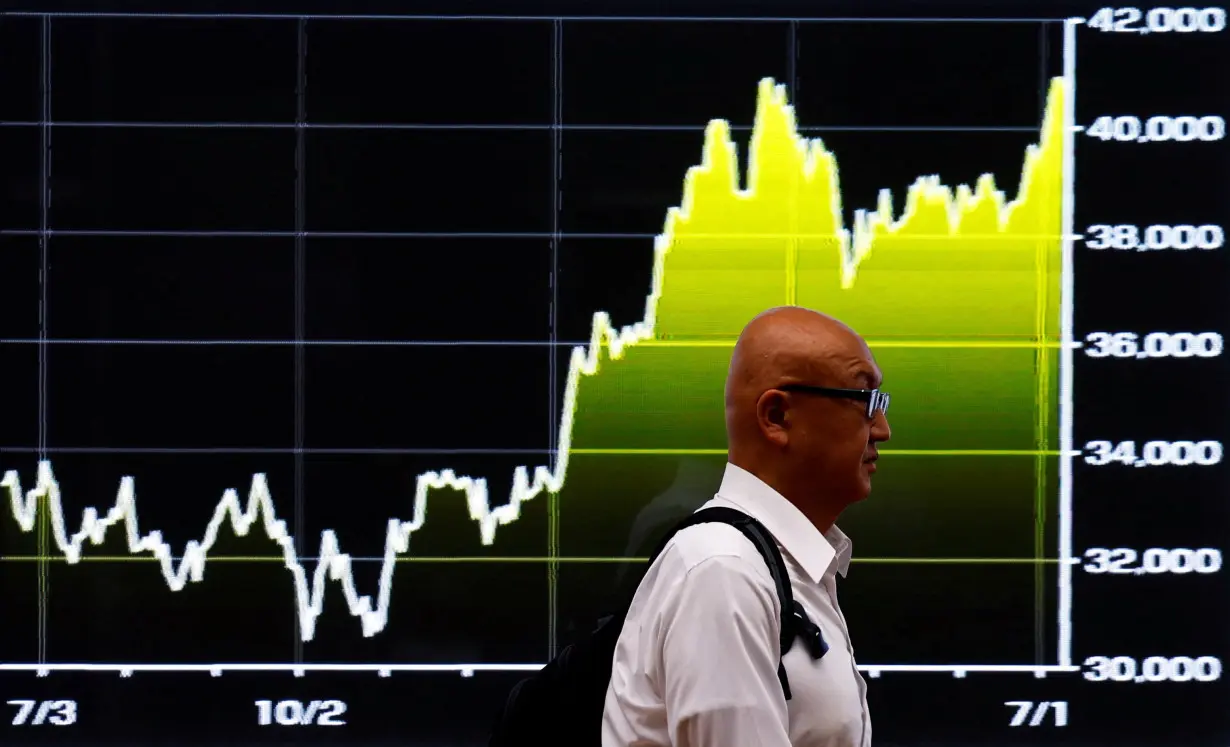 FILE PHOTO: A man walks past an electric screen displaying graph showing recent movements on Japan's Nikkei share average in Tokyo