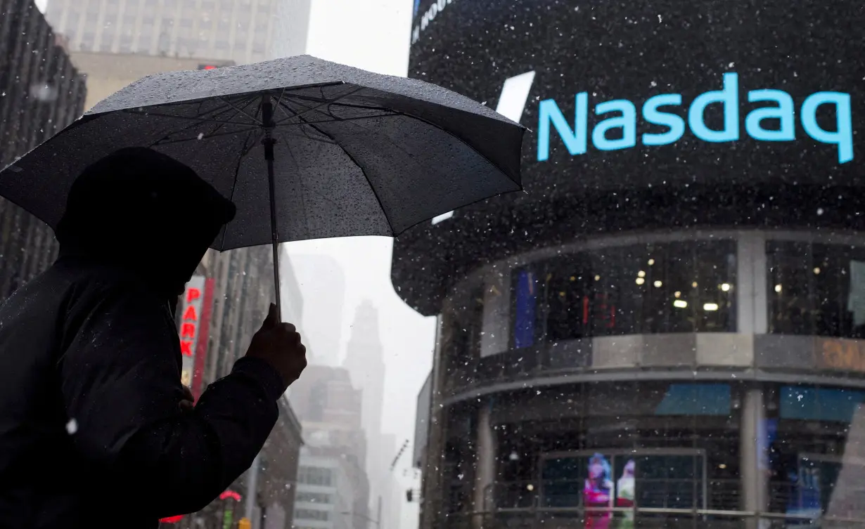 FILE PHOTO: A man uses an umbrella to guard against snowfall as he walks past the Nasdaq MarketSite in Times Square, Midtown New York