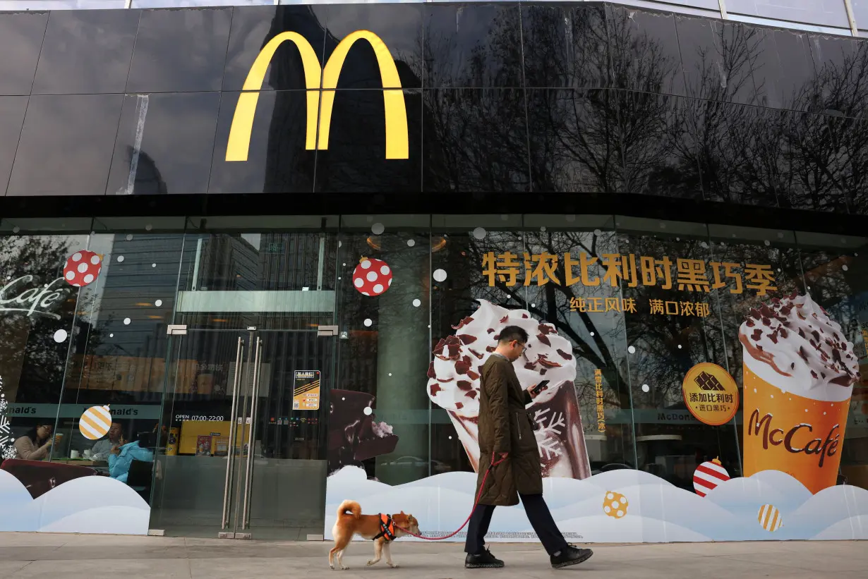 Man walks a dog past a McDonald's restaurant in Beijing