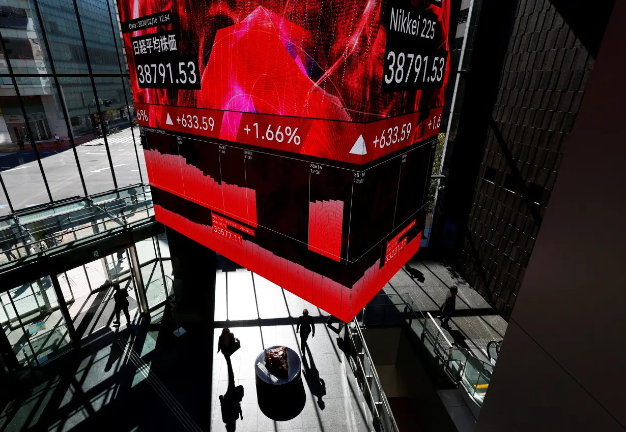 Visitors walk under a huge screen displaying Japan's Nikkei share average inside a building in Tokyo