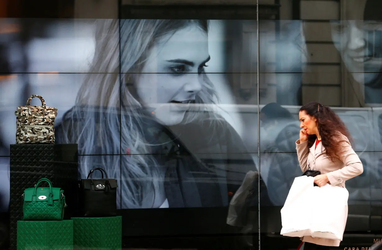 FILE PHOTO: A woman walks past a video display in the shop window of a Mulberry store in central London