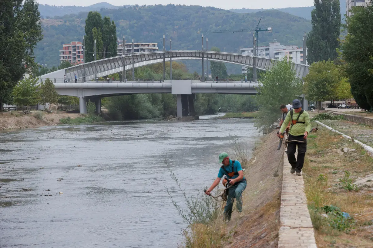 Workers cut grass near the main bridge, in Mitrovica