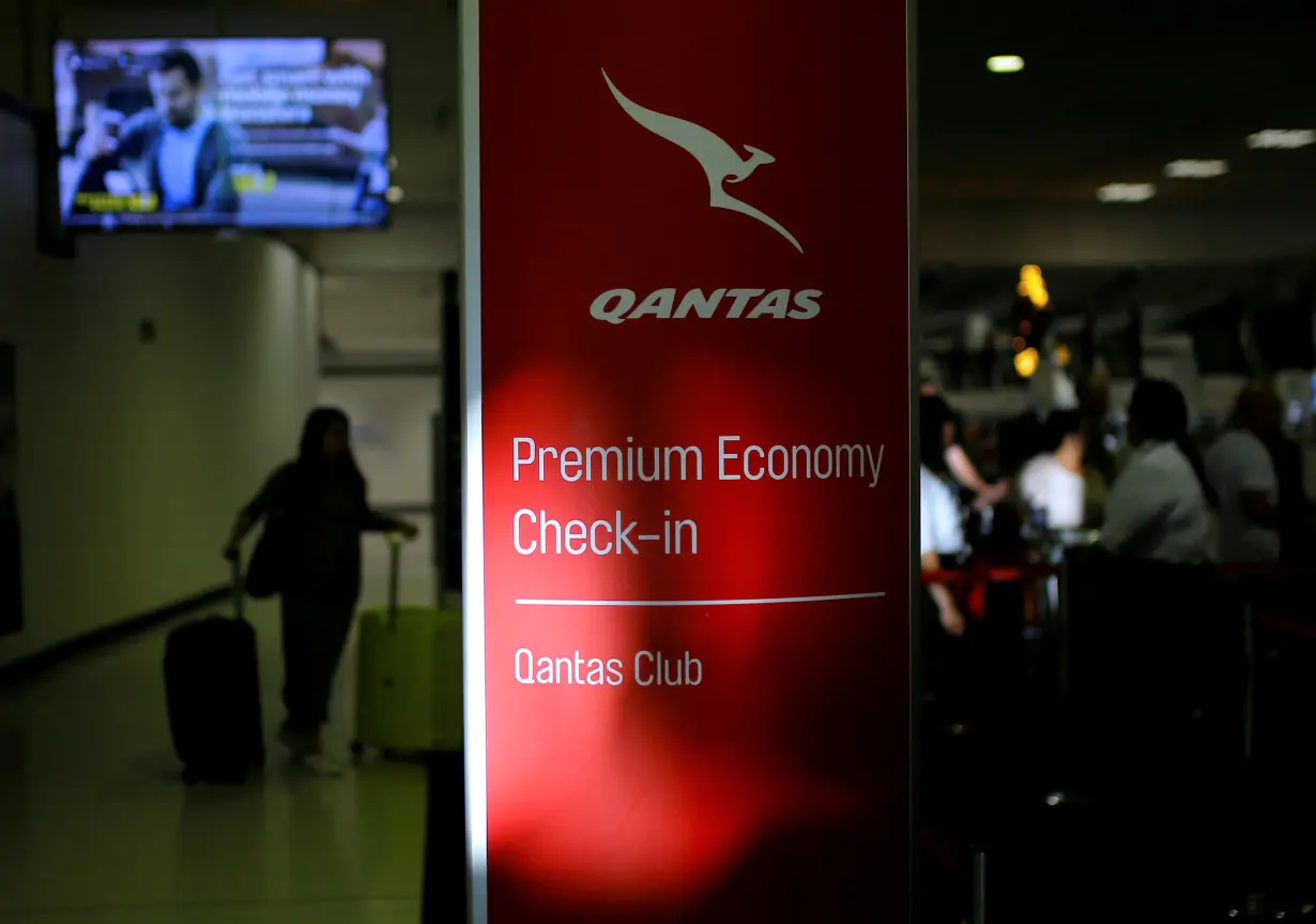 A passenger walks with their luggage as they approach a Qantas Airways check-in counter at Sydney International Airport