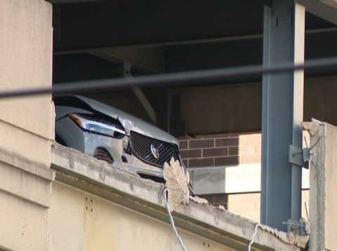 Vehicle partially hangs from parking garage after crashing into barrier