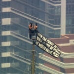 Two people scale to top of Empire State Building carrying banner